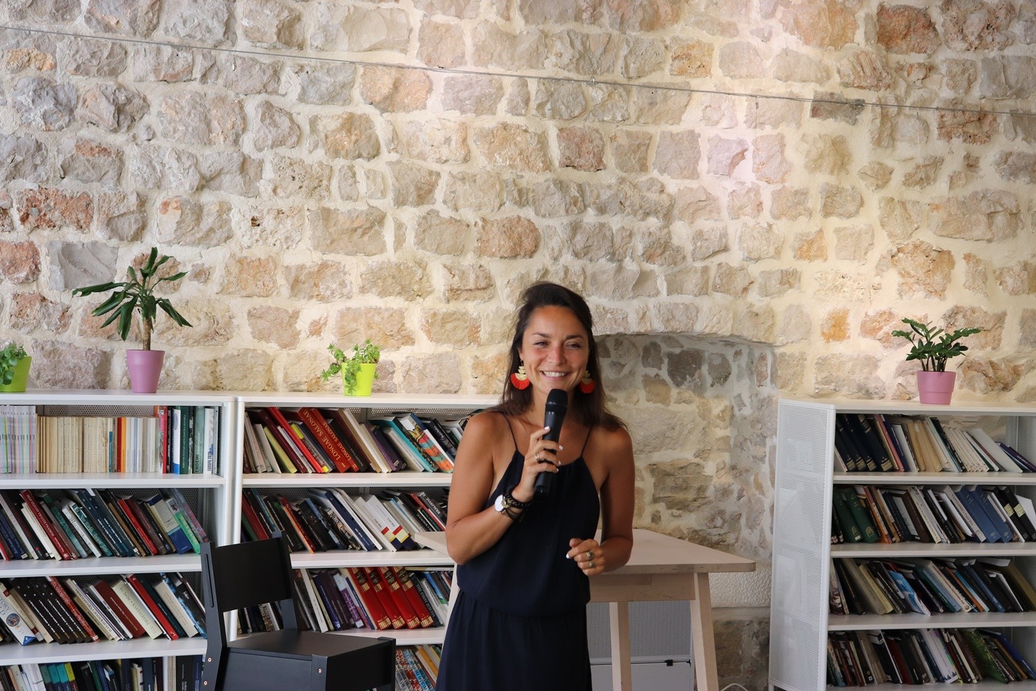 Smiling woman speaking into a microphone in a stone-walled library at a digital nomad workshop