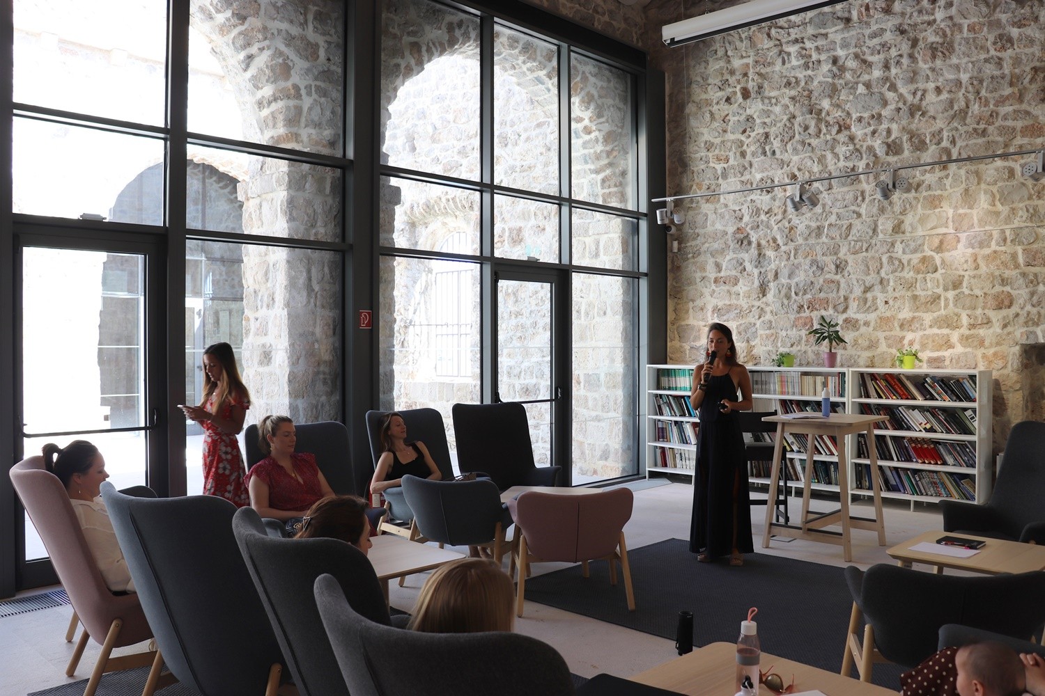 Woman giving a talk to a small audience seated in armchairs in a stone-walled library