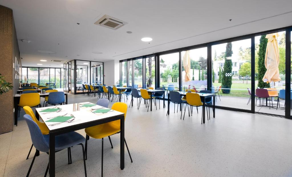 Bright café with yellow and blue chairs and glass walls onto a garden at Akademis Academia