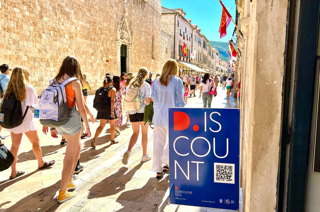 Young visitors walking down a sunny Old City street past a Dubrovnik Pass discount sign