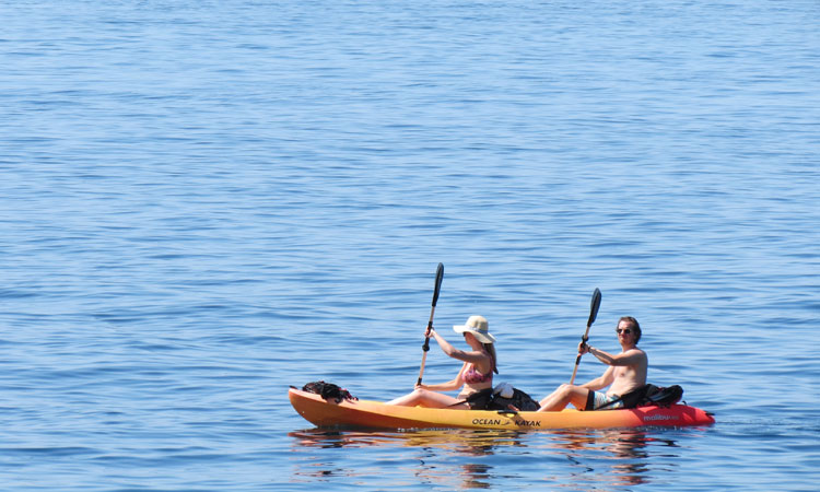 Two people paddling an orange kayak on calm blue sea