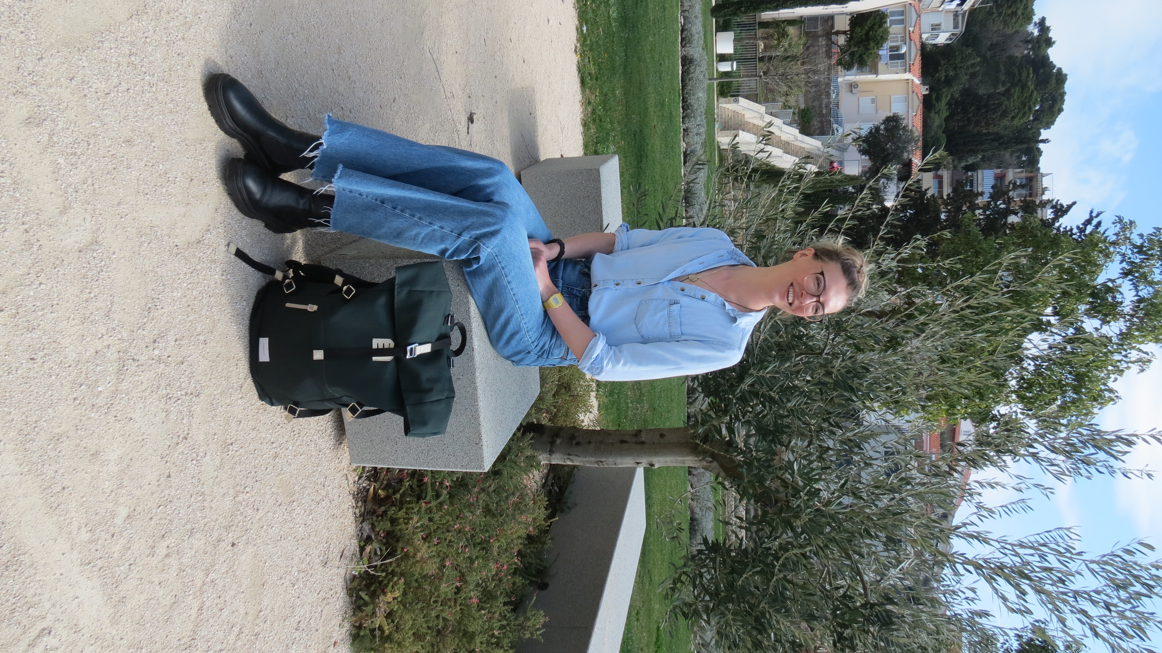 Helena Bradbury smiling on a stone bench next to an olive tree in a sunny Dubrovnik park