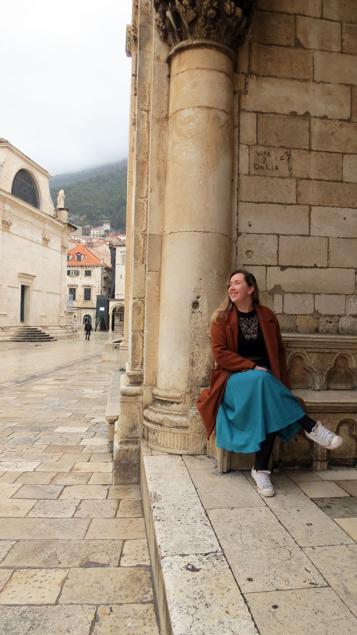 Han Talbot sitting at the foot of a stone column on a quiet, rain-washed street in Dubrovnik Old Town