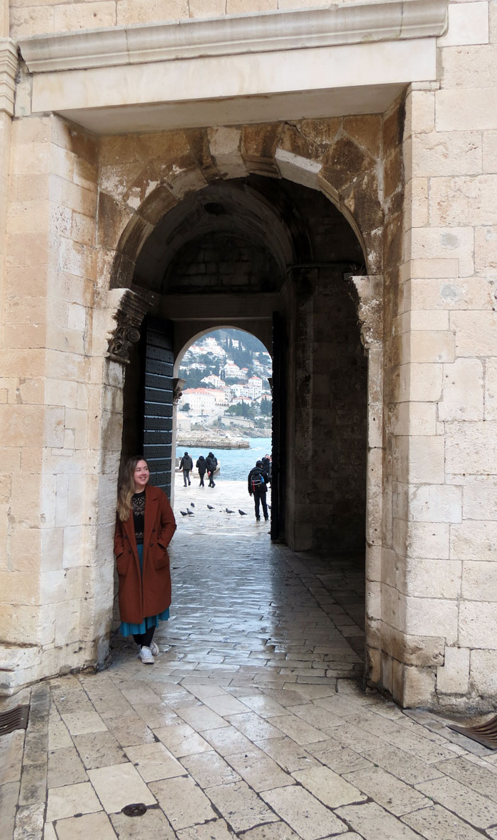 Han Talbot standing in a stone gateway of Dubrovnik's city walls with the sea beyond