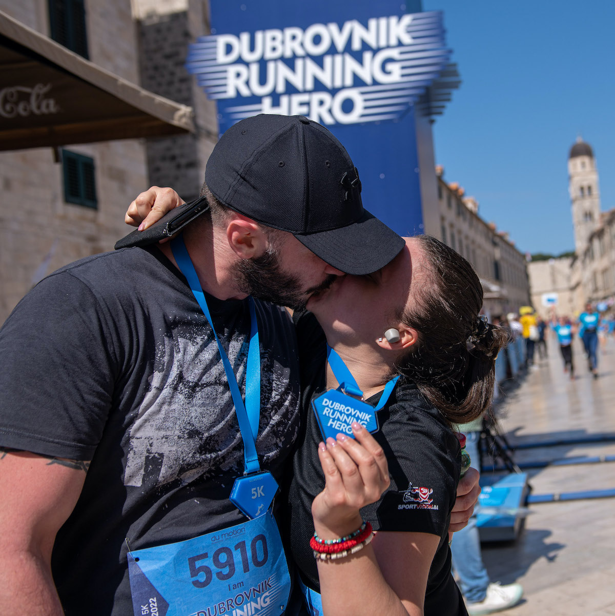 Couple kissing on Stradun after the race, holding a Dubrovnik Running Hero 5K medal