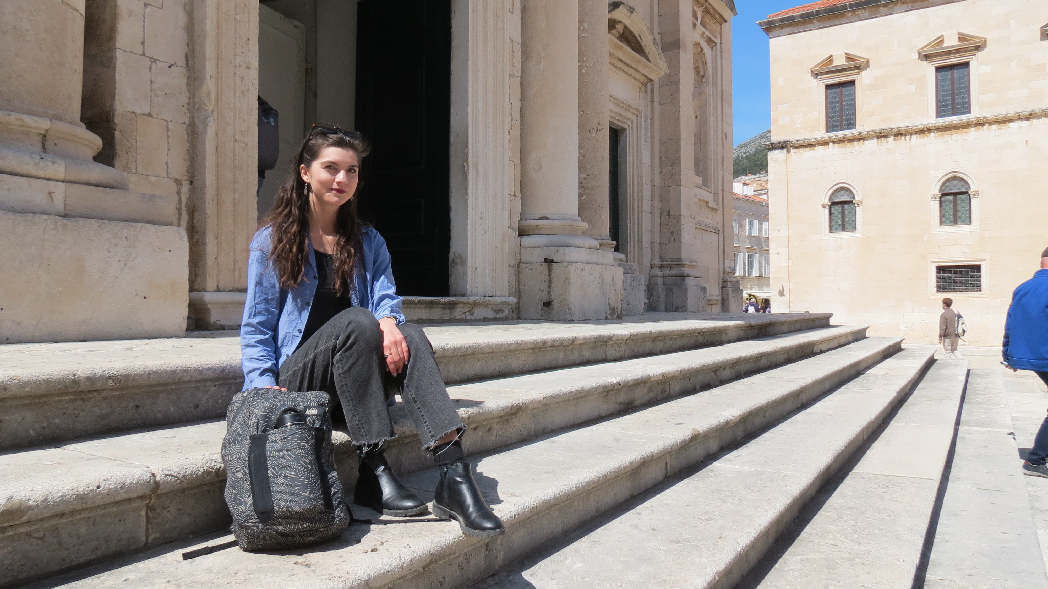 Yvonne Worden sitting on the stone steps of a church in Dubrovnik Old Town with her backpack