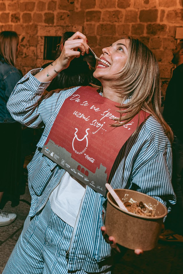 Woman in a Bavarin bib tasting food from a paper bowl at the street food festival