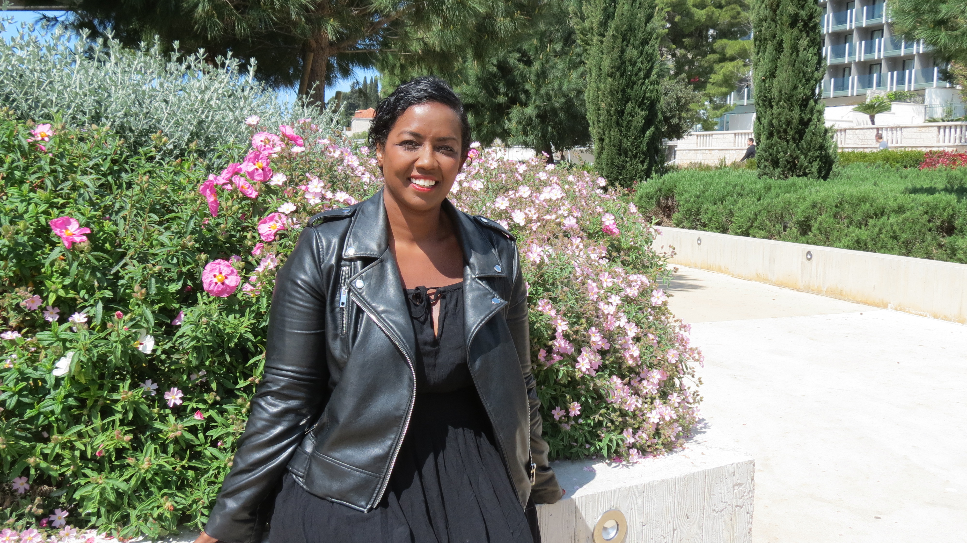 Mita Carriman smiling in front of a flowering shrub on a sunny day in Dubrovnik