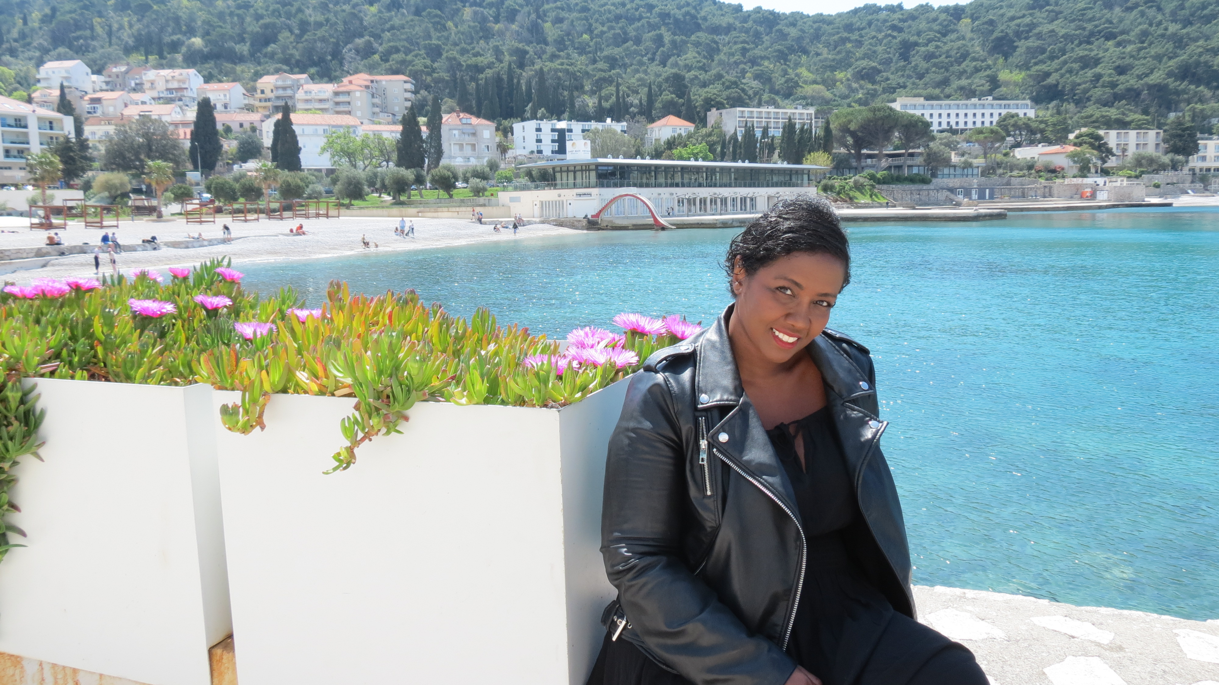 Mita Carriman sitting by flower planters above a turquoise bay in Dubrovnik
