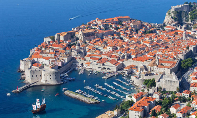 Aerial view of Dubrovnik Old Town, its walls and harbour, with a sailing ship on the sea