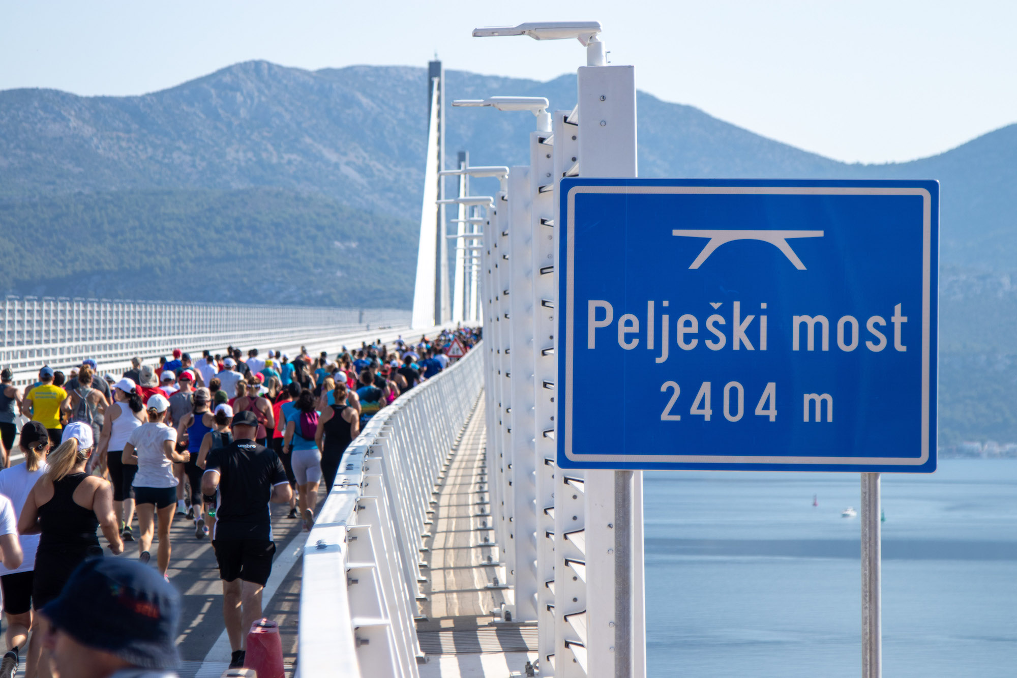 Runners crossing the Pelješac Bridge past a sign reading Pelješki most 2404 m