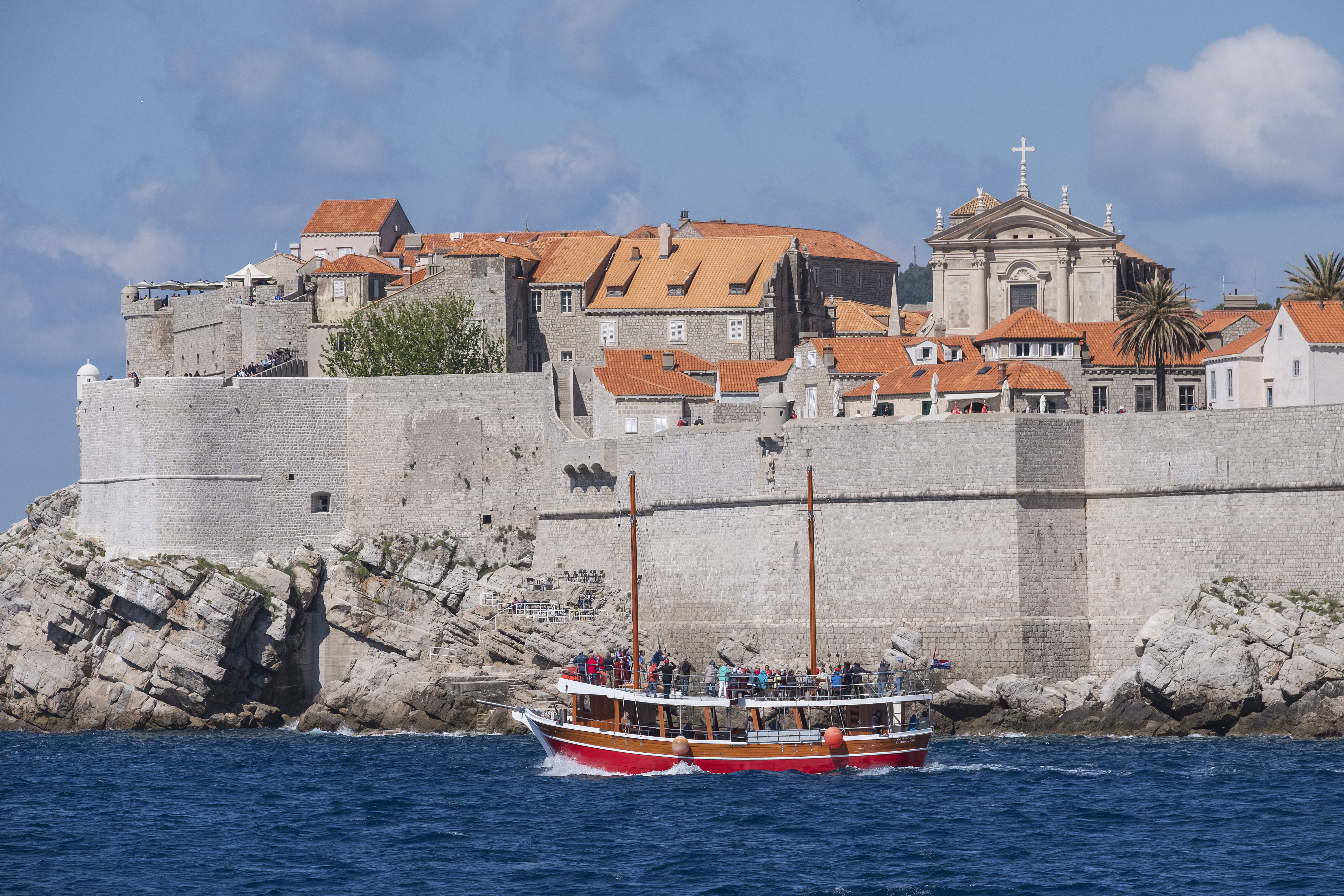 Tourist boat sailing past Dubrovnik's City Walls and Old Town rooftops