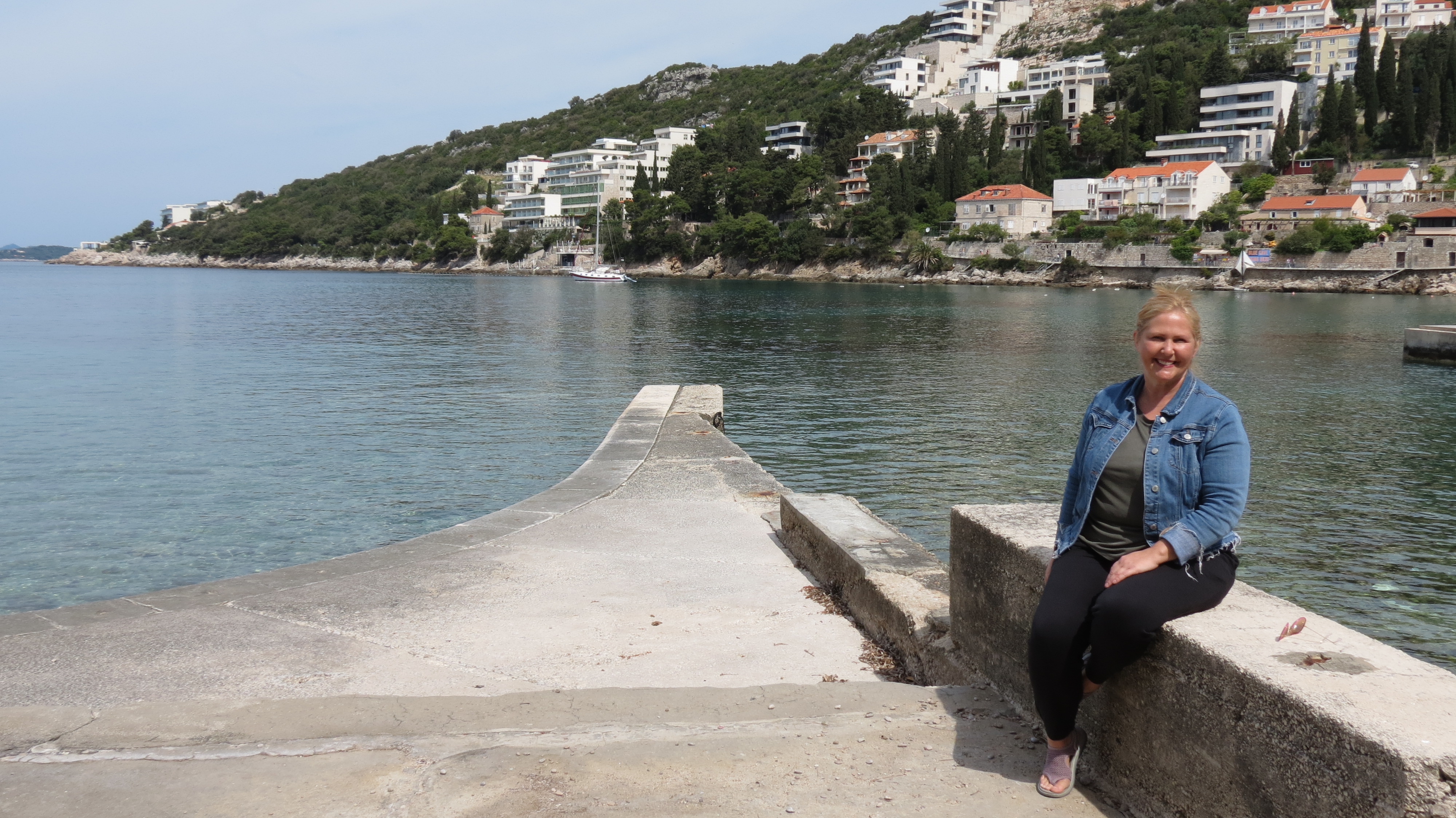 Kristie Sullivan sitting on a stone pier by a calm bay in Dubrovnik