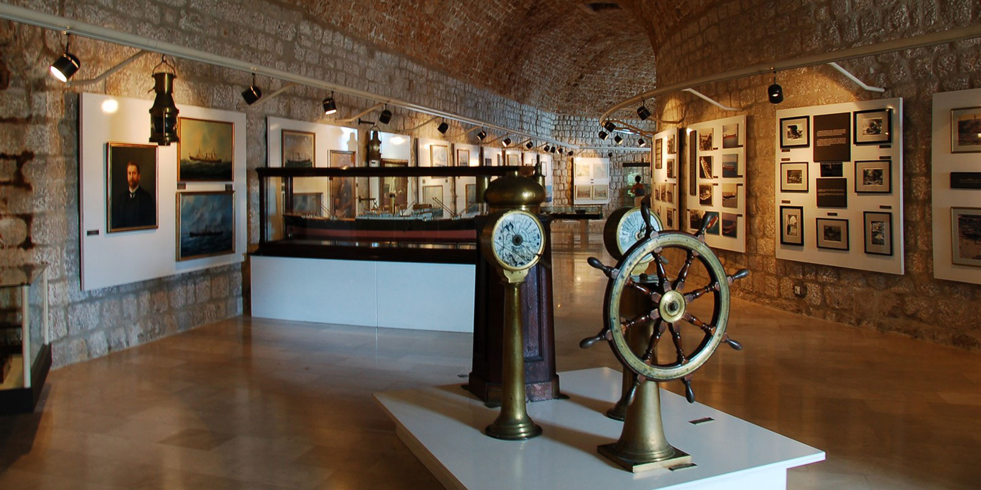 Maritime Museum gallery in a stone vault with ship's wheels, a binnacle and maritime portraits