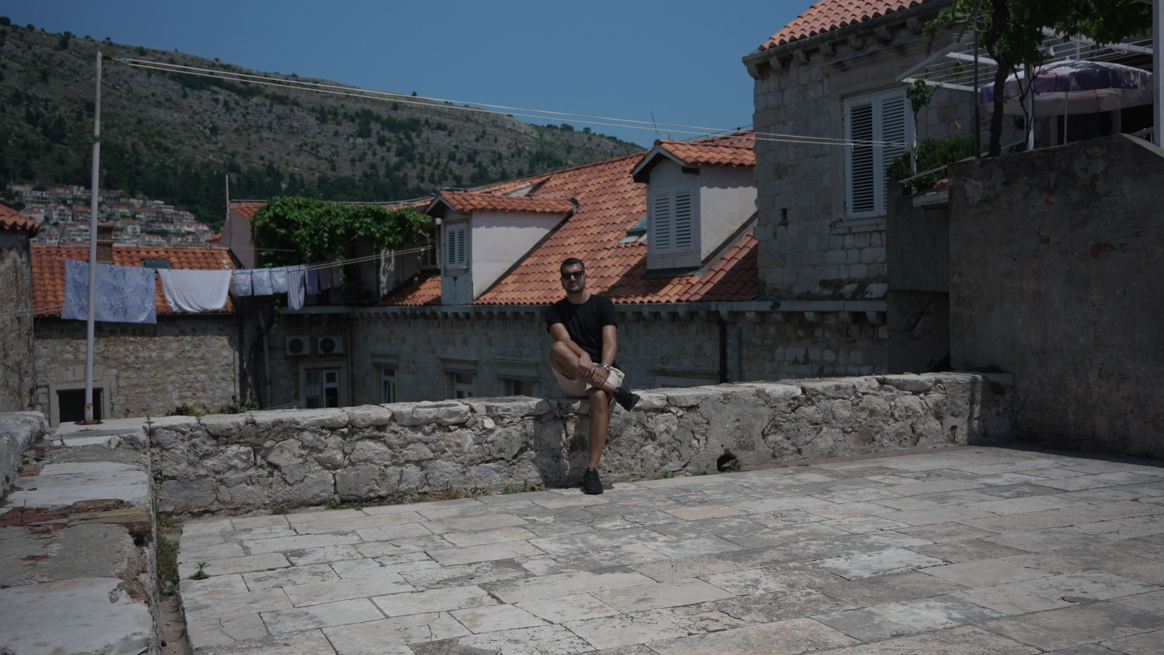 Daniel Hogston sitting on a low stone wall on a terrace among Old Town rooftops and drying laundry