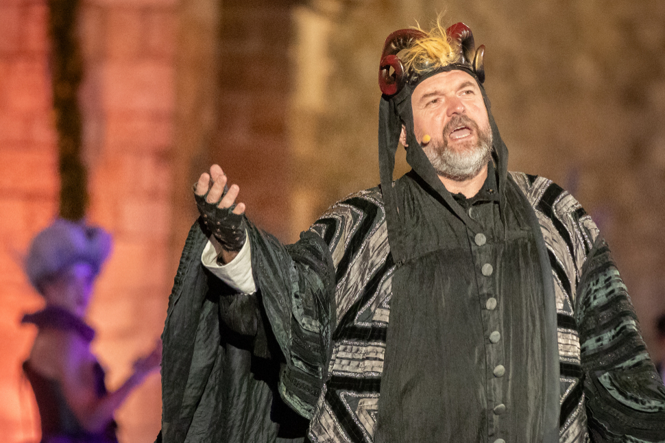 Actor in a dark costume with a horned headdress performing at the Summer Festival opening ceremony