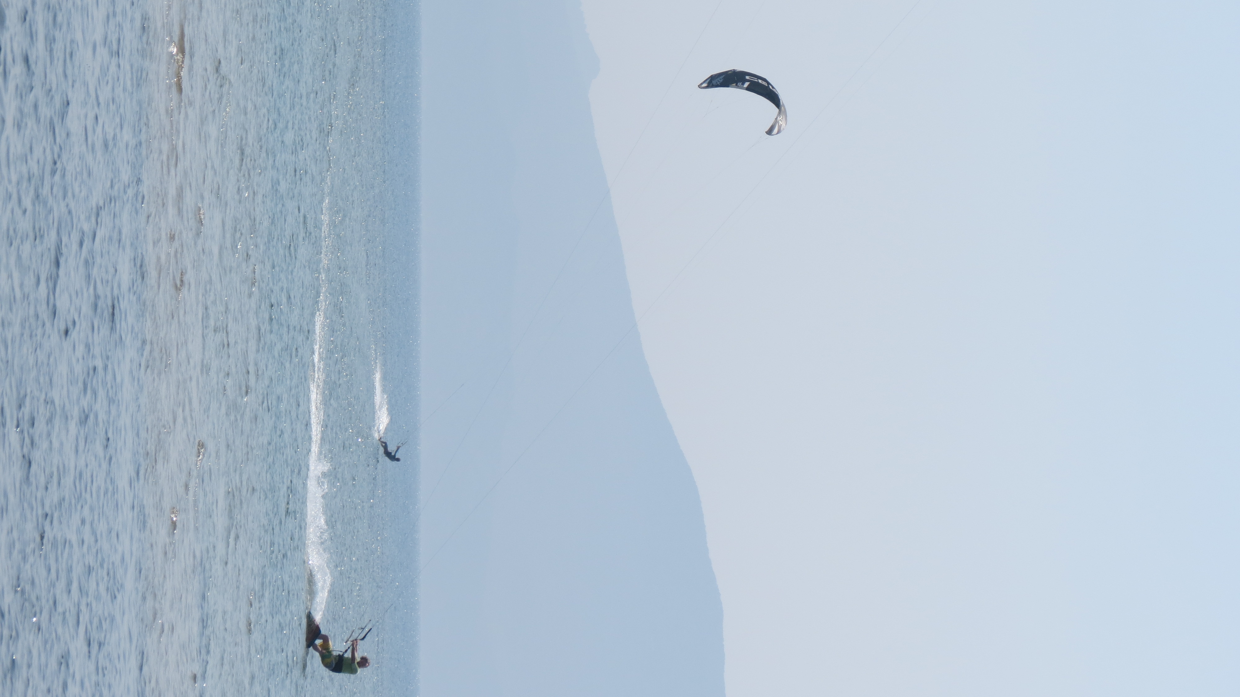 Kite surfers skimming the sea beneath hazy mountains at the Neretva River mouth