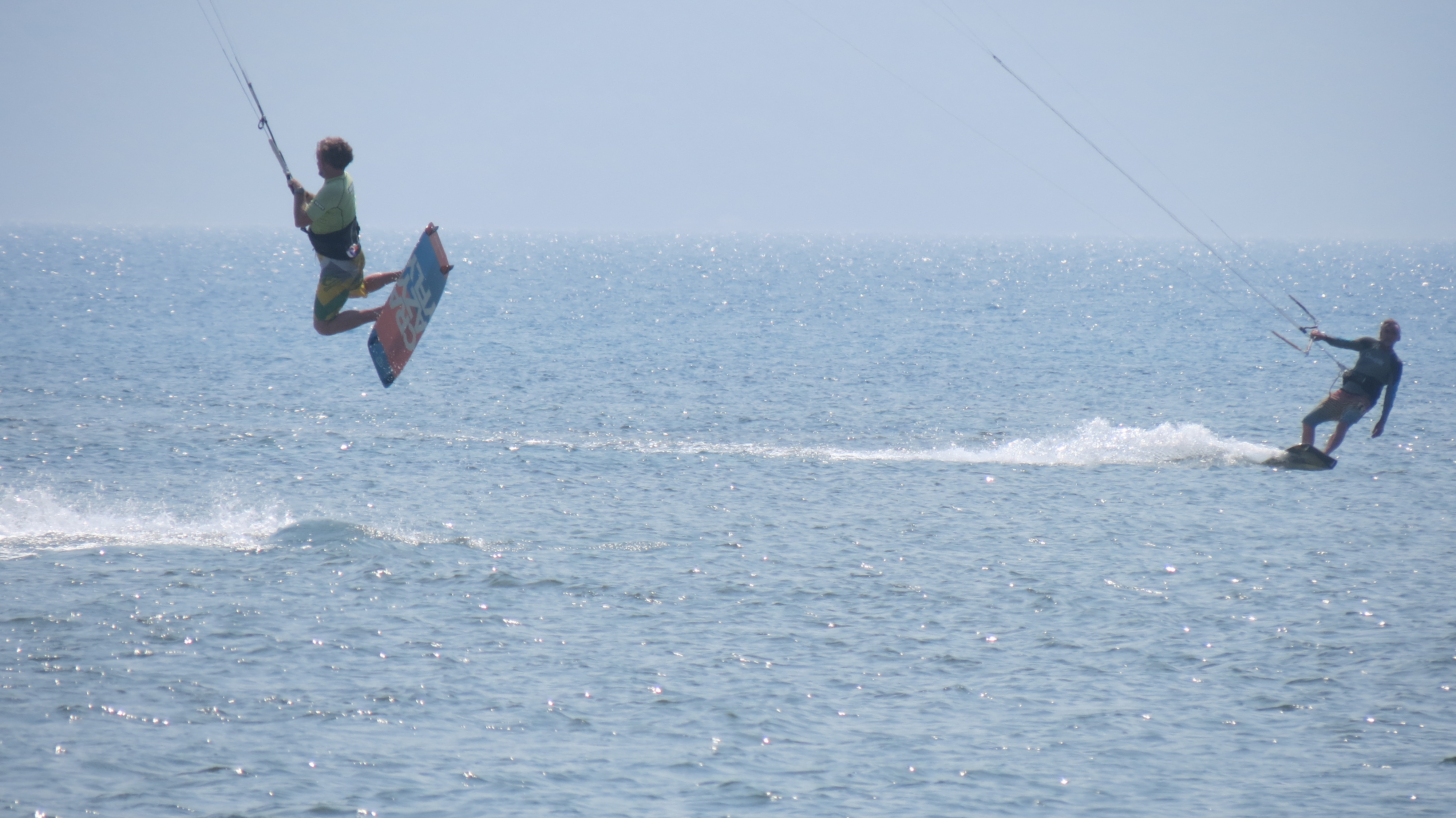 Two kite surfers on the sea at the Neretva River mouth, one jumping high into the air