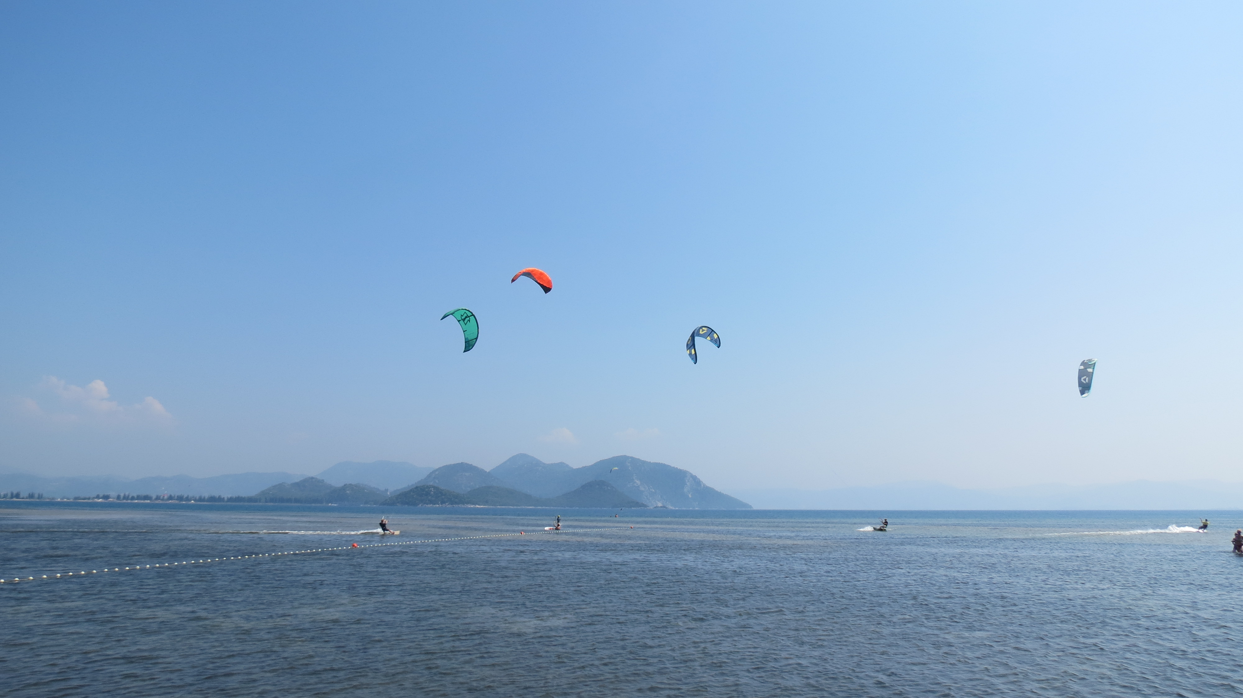 Colourful kites above kite surfers on the calm sea at the Neretva River mouth, hills in the distance