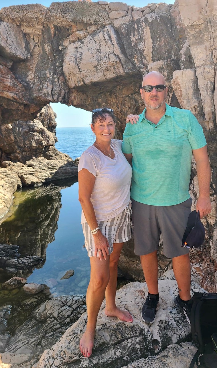 Marlee McCormick and Jeff Burkett posing under a natural rock arch by the sea on Lokrum