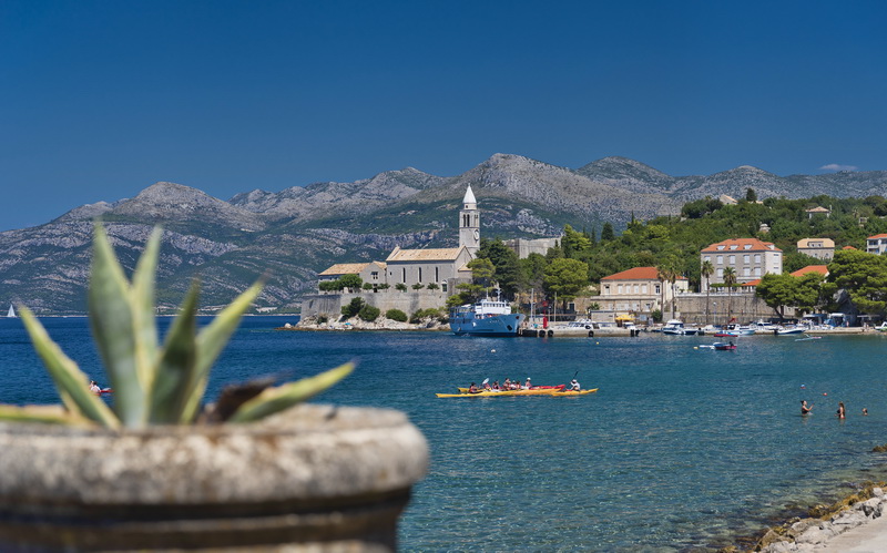 Lopud harbour with a church bell tower, kayakers and mainland mountains behind