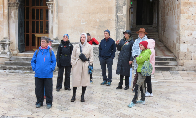 Tour group in winter coats listening to a guide in front of a stone church in Dubrovnik Old Town