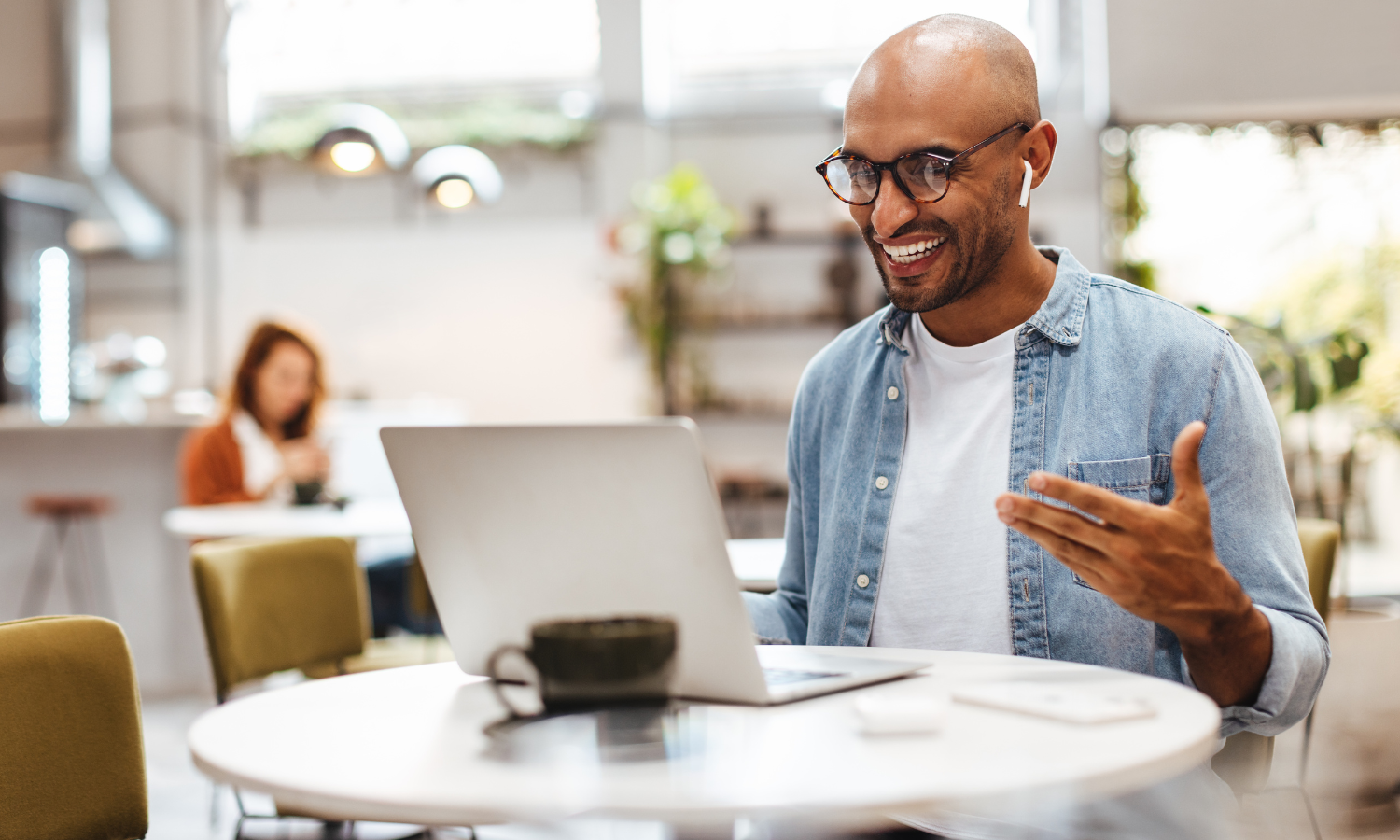 Smiling man with glasses on a video call at his laptop in a café-style workspace