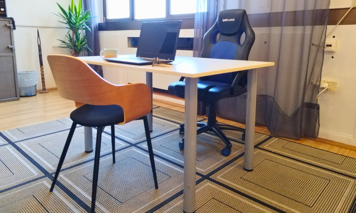 Desk with a laptop and coffee mug, a wooden chair and a gaming-style office chair in the TUP co-working space