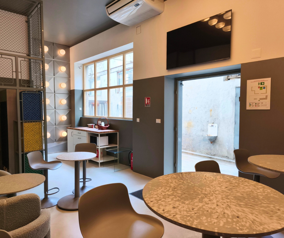 Offline Space lounge with round tables, a wall TV, kitchenette and an open door to the courtyard