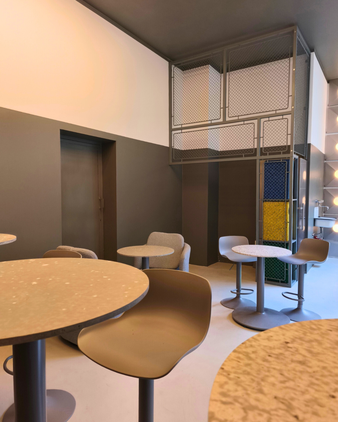 Offline Space interior with round tables, grey stools, an armchair and a steel mesh loft structure