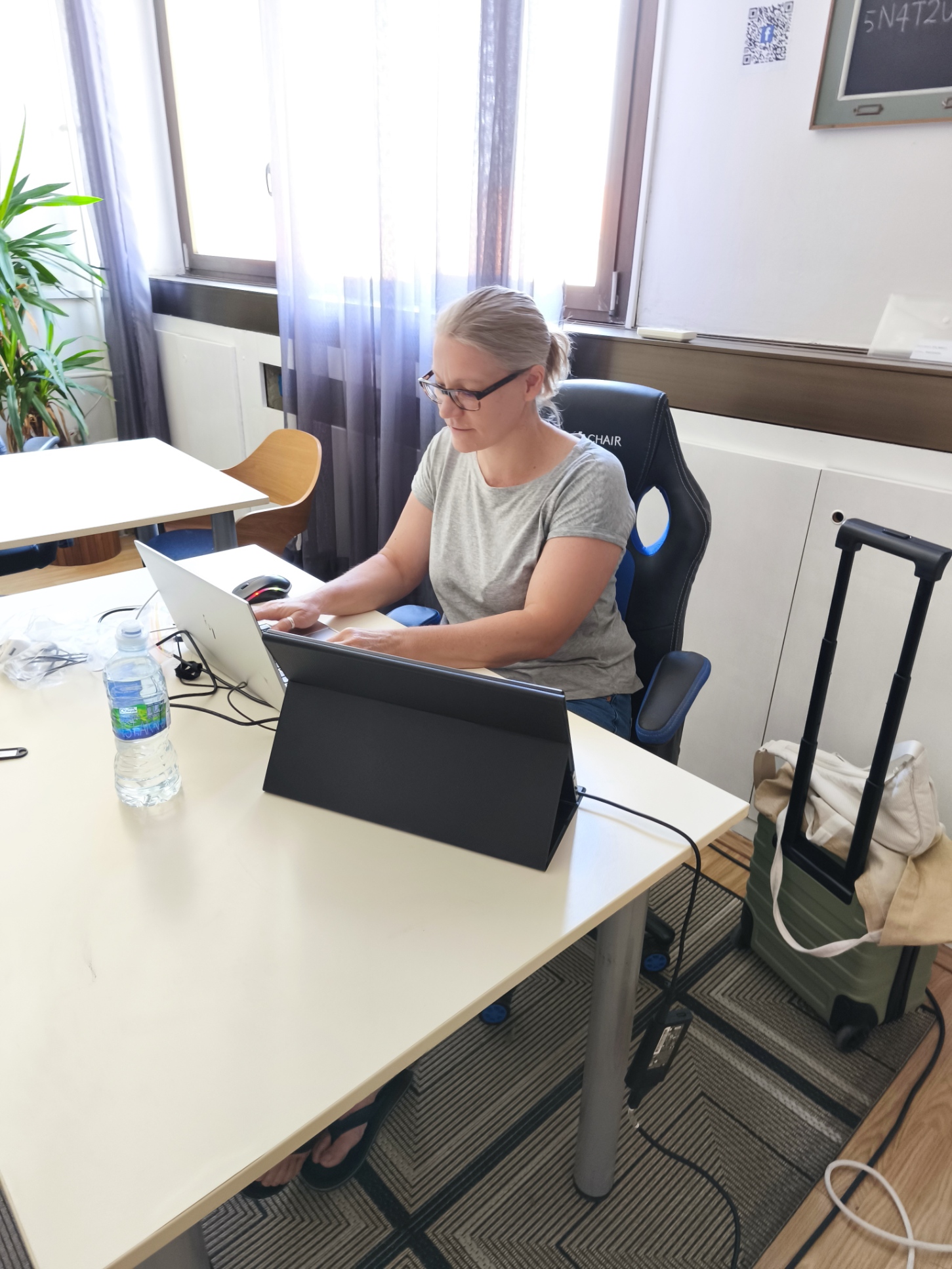Woman working on a laptop and tablet in Dubrovnik's free co-working space, a suitcase beside her