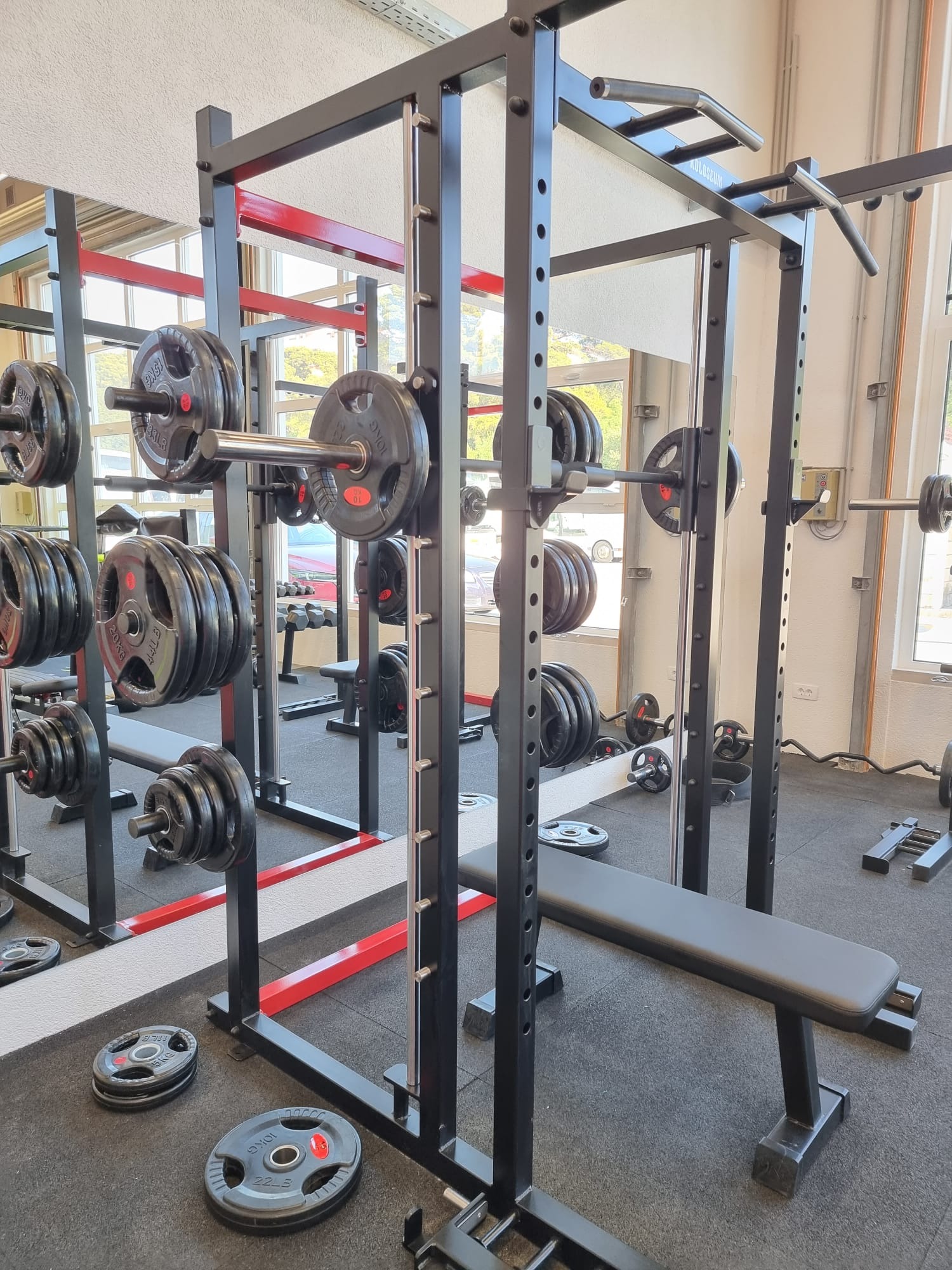 Power rack with weight plates and a flat bench reflected in a gym mirror