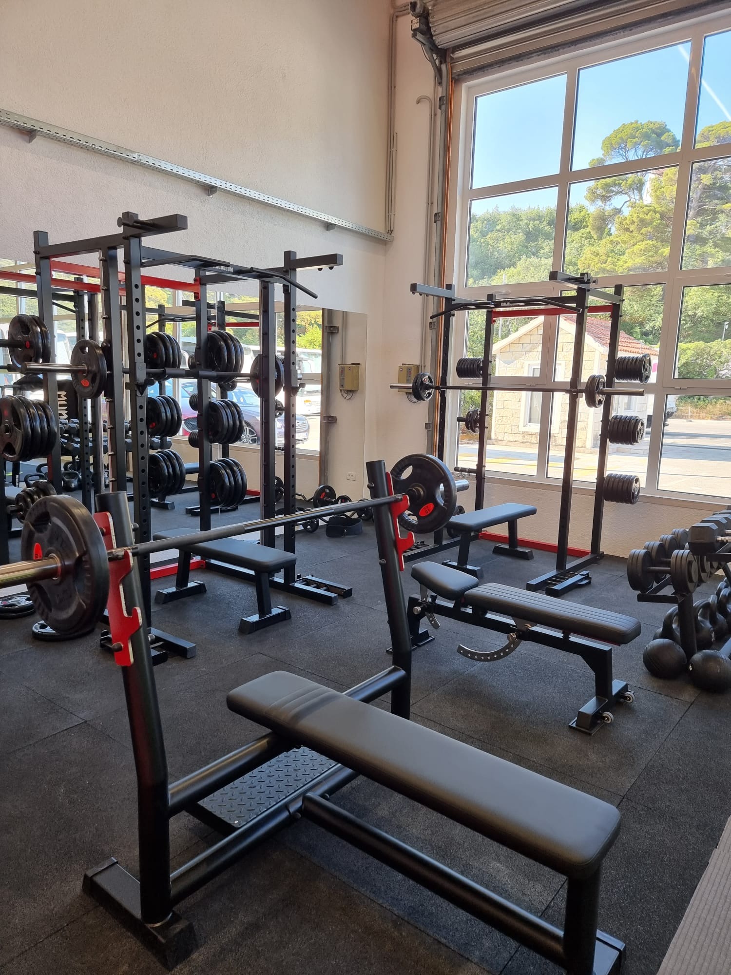 Squat racks, benches and barbells in a gym with large windows