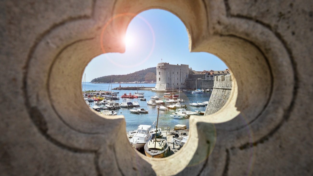 Dubrovnik old harbour and St John's Fortress seen through a four-leaf opening in a stone wall