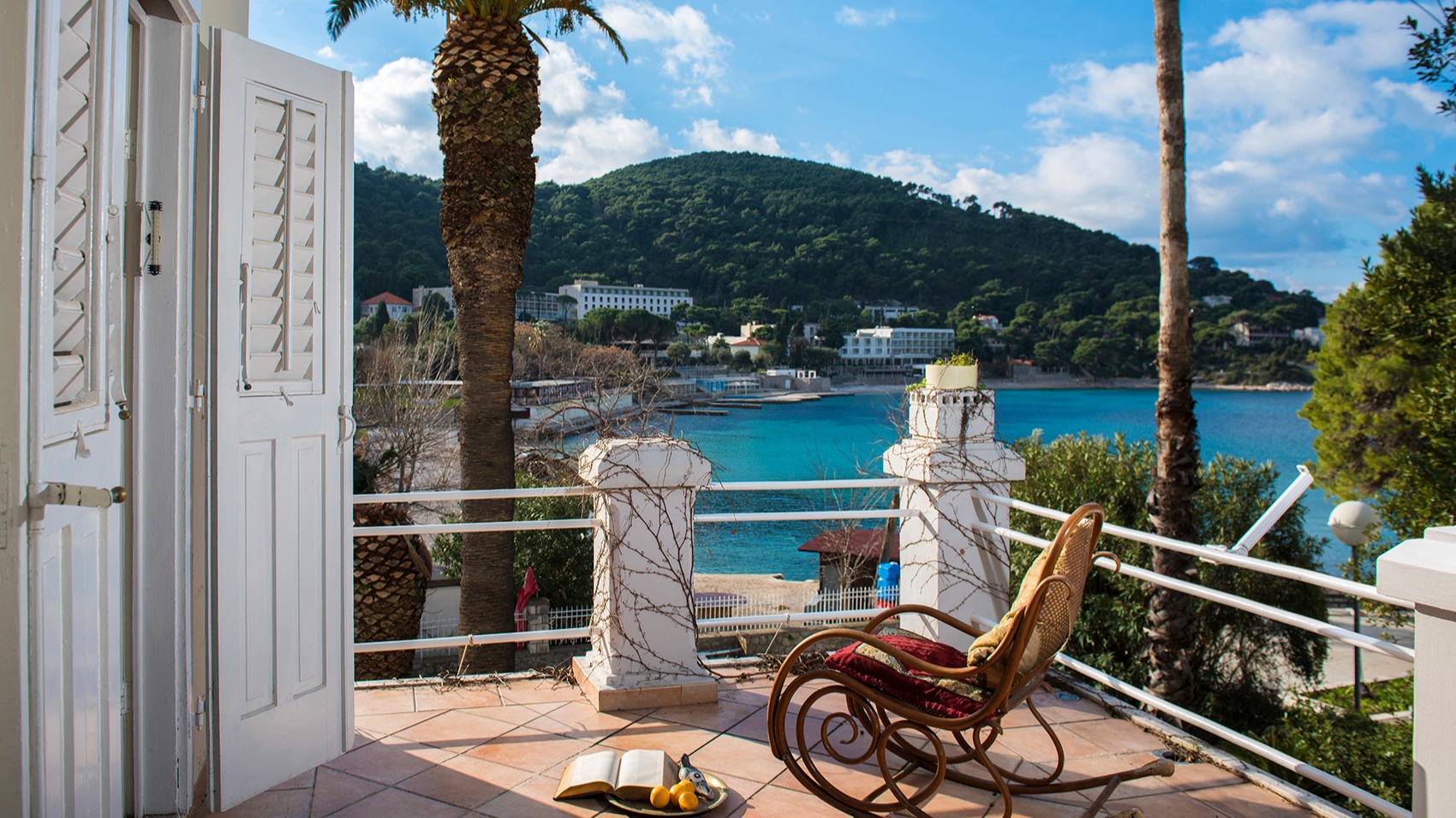 Terrace with a rocking chair and palm trees overlooking the bay and green hill in Lapad