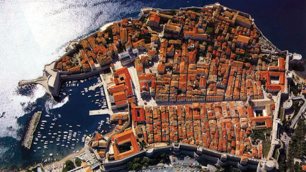 Aerial view of the red rooftops of Dubrovnik Old City inside its walls, next to the old harbour